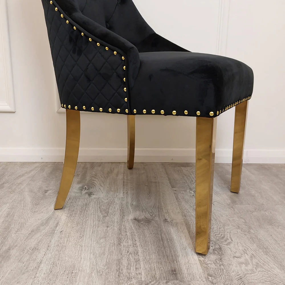 Black velvet lion knocker dining chair with gold detailing, quilted back, and studded trim, styled with a marble and gold dining table in a luxury setting.