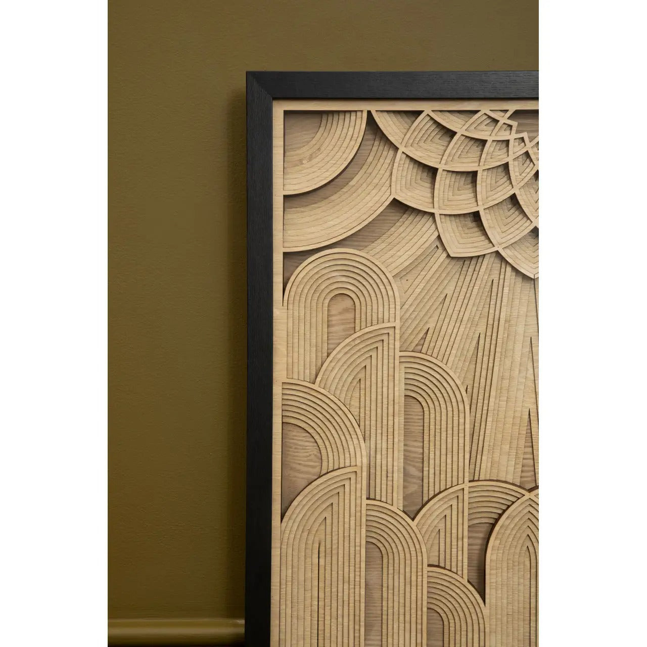 Wooden wall art with geometric pattern in a black frame against a green wall.