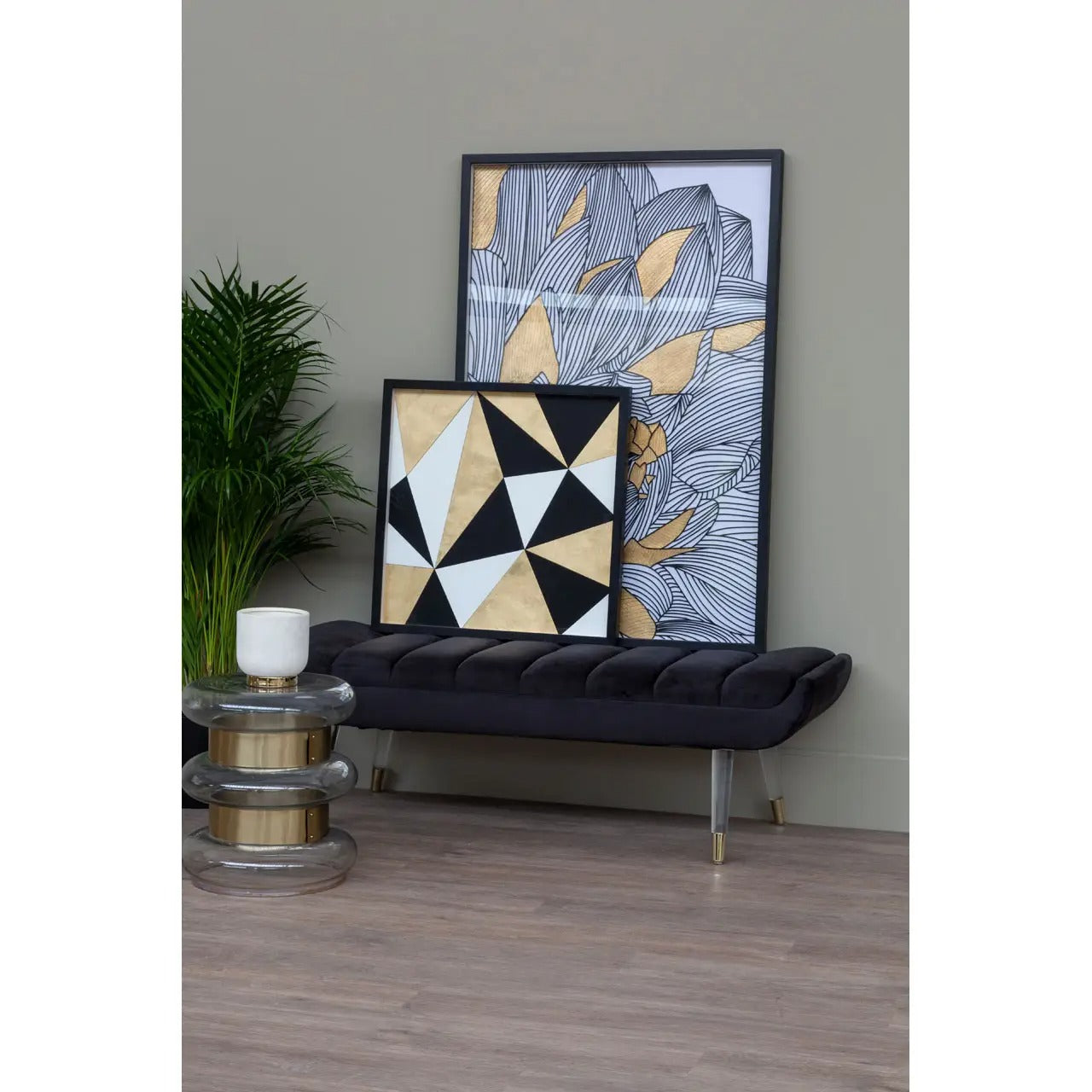 Two framed artworks on a wall with a black cushioned chair and small table.
