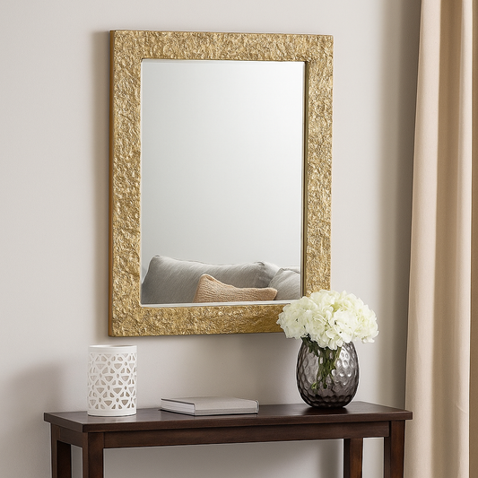 Decorative gold-framed mirror on a wall with a table below holding a vase and flowers.