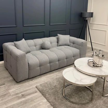 Grey bouclé 3 seater sofa with deep tufting and soft curved design, styled in a contemporary living room with round marble coffee tables and minimalist decor.