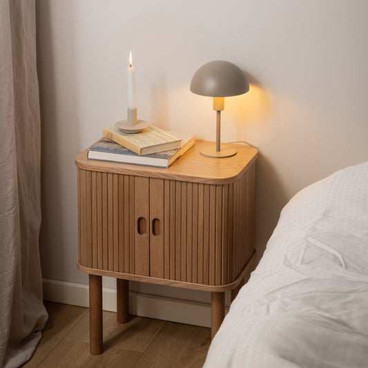 Modern oak bedside table with vertical slatted tambour doors, rounded corners, and compact square design, styled in a minimalist bedroom setting.