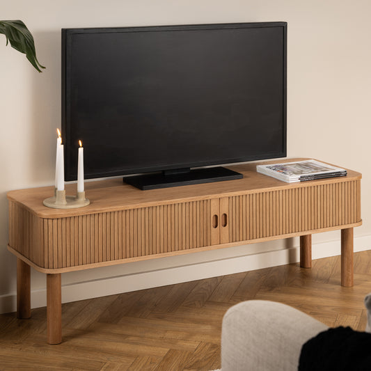 Oak TV stand with rounded edges and vertical slatted tambour doors, featuring a natural lacquered finish, styled with a TV and candles in a Scandinavian living room.