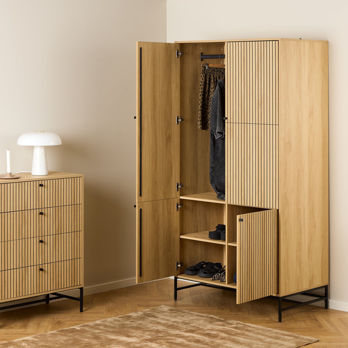 Large oak wardrobe with 4 vertically slatted doors and black steel base, opened to reveal hanging space and shelves, styled in a modern Scandinavian bedroom.