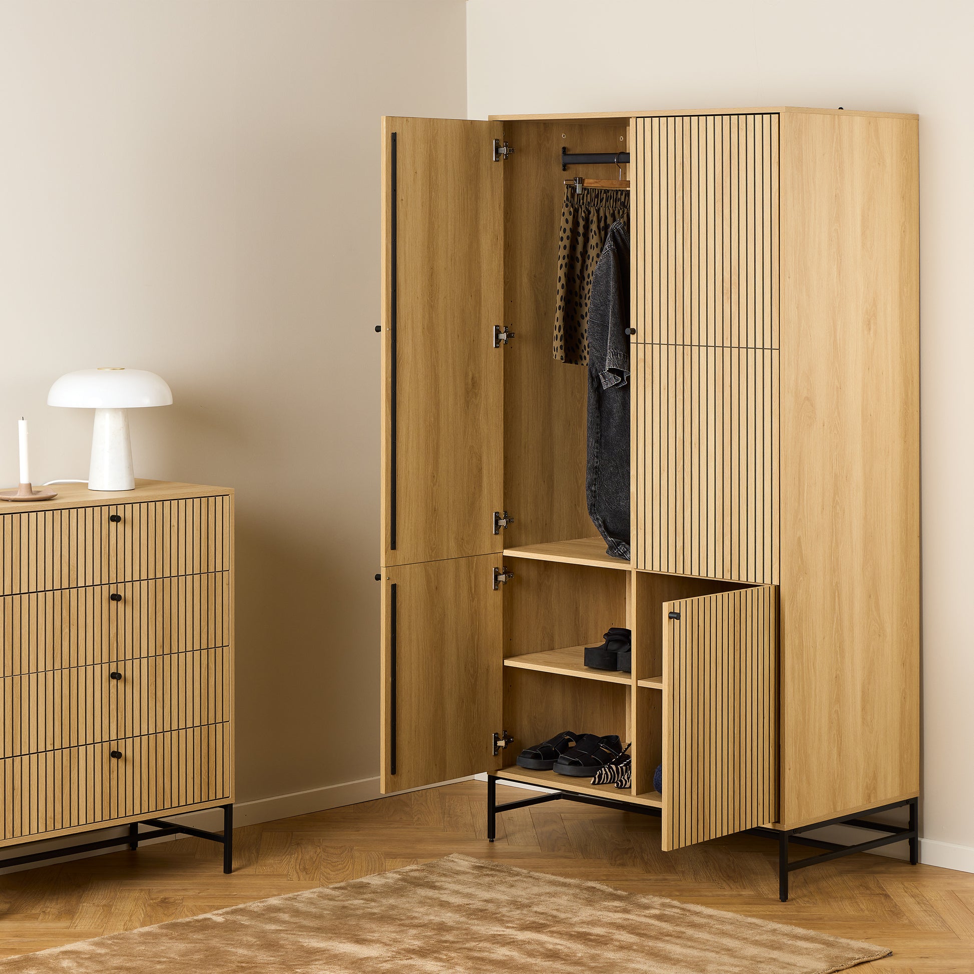 Large oak wardrobe with 4 vertically slatted doors and black steel base, opened to reveal hanging space and shelves, styled in a modern Scandinavian bedroom.