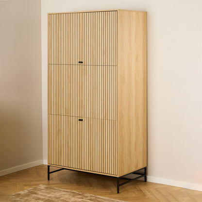 Large oak wardrobe with 4 vertically slatted doors and black steel base, opened to reveal hanging space and shelves, styled in a modern Scandinavian bedroom.
