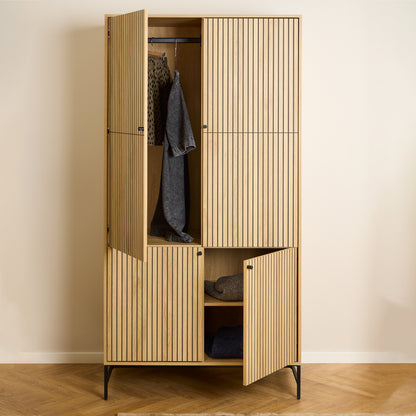Large oak wardrobe with 4 vertically slatted doors and black steel base, opened to reveal hanging space and shelves, styled in a modern Scandinavian bedroom.