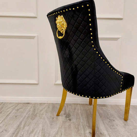 Black velvet lion knocker dining chair with gold detailing, quilted back, and studded trim, styled with a marble and gold dining table in a luxury setting.